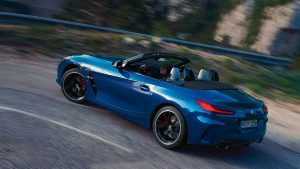 Blauer BMW Z4 Cabrio fährt auf kurviger Straße; Bäume im Hintergrund.